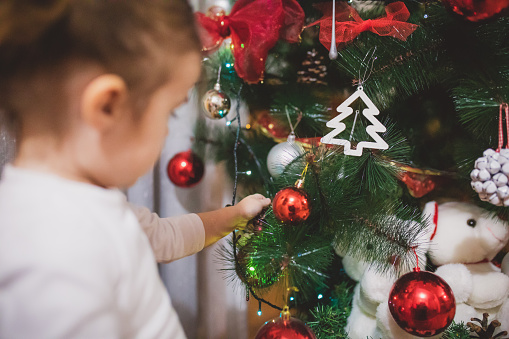 A cute little girl in a decorates the Christmas tree with tree decorations.