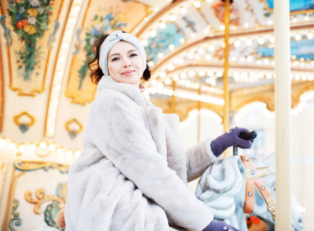 Beautiful and cheerful brunette woman in a fur coat rides on a carousel stock photo