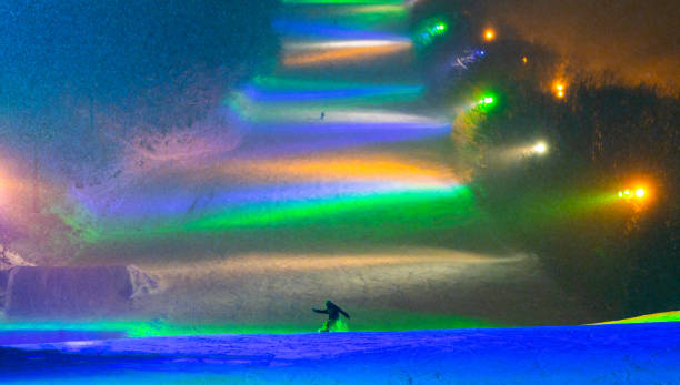 A snowboarder enjoys snowboarding at night time under colorful lights.