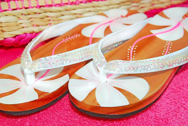 Pretty flip flop sandals with sequins on towel next to beach bag