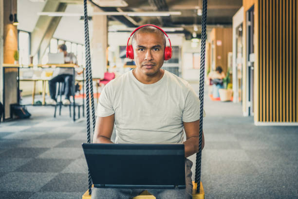 istock Portrait of entrepreneur working on an office swing while using head phones 1452410522