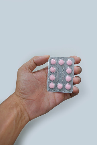 picture of an asian man hand holding a pack of pink pills isolated on white background.