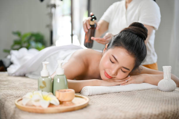 Relaxed Asian woman lying on massage table, receiving body massage, enjoying Thai spa at salon. stock photo