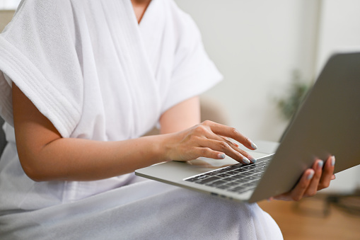 cropped images, A female in bathrobe using laptop computer, typing on keyboard, work from home.