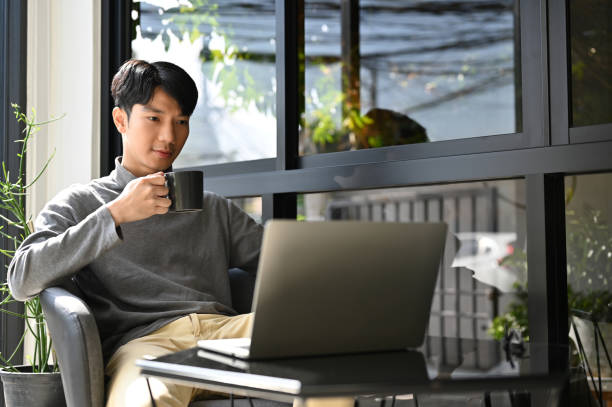 istock Smart Asian male freelancer sipping coffee, using laptop while remote working at the cafe. 1452420653
