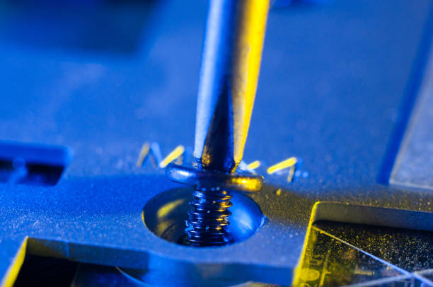 Unscrewing a small screw with a Phillips screwdriver close-up from a laptop case, yellow-blue lighting