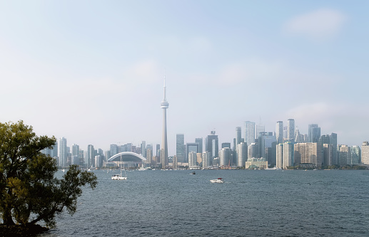 The Toronto skyline by Lake Ontario on a hazy late summer day in Toronto, Ontario, Canada. Boats can be seen on the calm water.