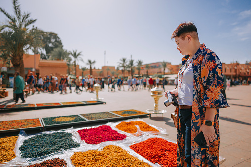 Curious Asian Chinese female tourist looking at colourful dried flowers on a market in a bazaar in Marrakech, Morocco, North Africa