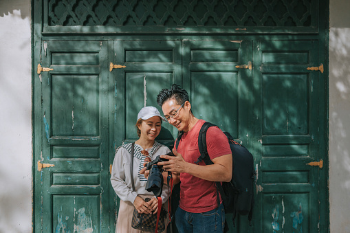 Asian Chinese couple tourist checking image captured with LCD screen of camera in front of islamic architecture building wooden door