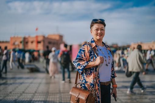 Asian Chinese female tourist standing looking at camera smiling  in front of Djemaa El Fna Square, Marrakech, Morocco