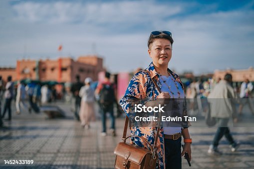 istock Asian Chinese female tourist standing looking at camera smiling  in front of Djemaa El Fna Square, Marrakech, Morocco 1452433189
