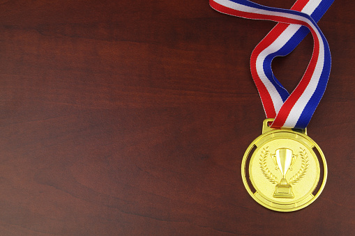 Gold medal with multicolored ribbon on wooden background, copy space for text.
