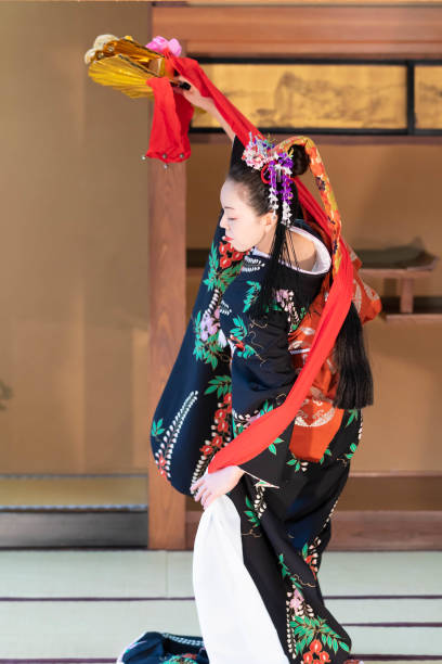 widok z tyłu młodej japonki, z ozdobą włosów, w kimonie we wzory kwiatów, tańczącej japoński tradycyjny taniec z udekorowanym wachlarzem w japońskim pokoju - flowerpatterned zdjęcia i obrazy z banku zdjęć