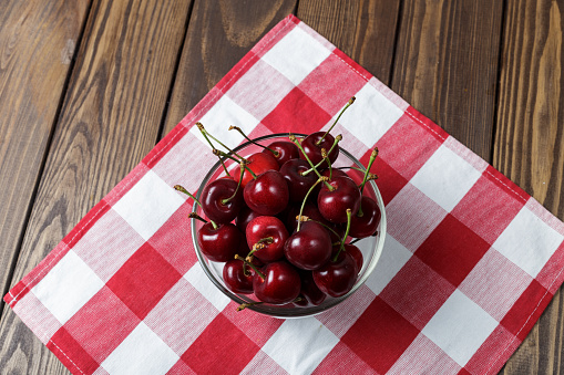 sweet cherry in a transparent bowl on a wooden background. plate on a red napkin. copy space