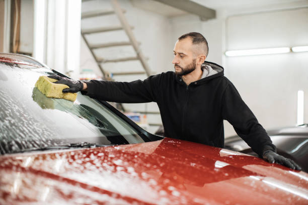 istock Young handsome bearded man worker washing soapy car windshield with sponge on a car wash station. 1452439997