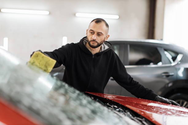 istock Young handsome bearded man worker washing soapy car windshield with sponge on a car wash station. 1452439998