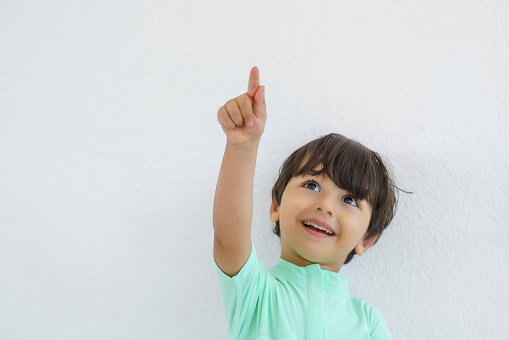 Portrait of amazed cute little boy pointing to empty place on white background