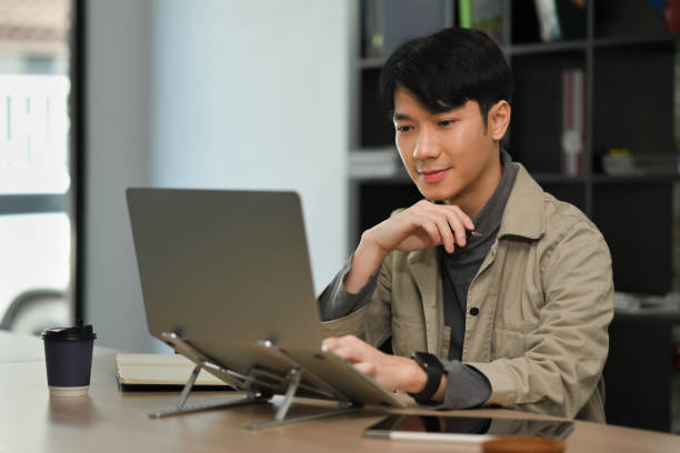 istock Handsome asian male freelancer working on design project online on laptop computer. 1452442127