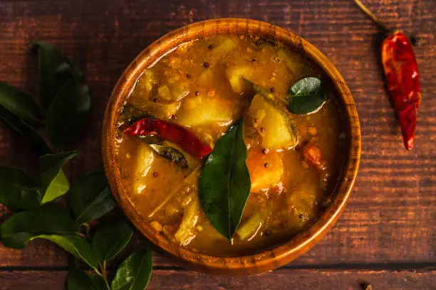 Photo of Sambar, a mixed vegetarian curry arranged on a wooden bowl on a wooden background. Sambar is popular in South India and Sri Lanka cuisines.