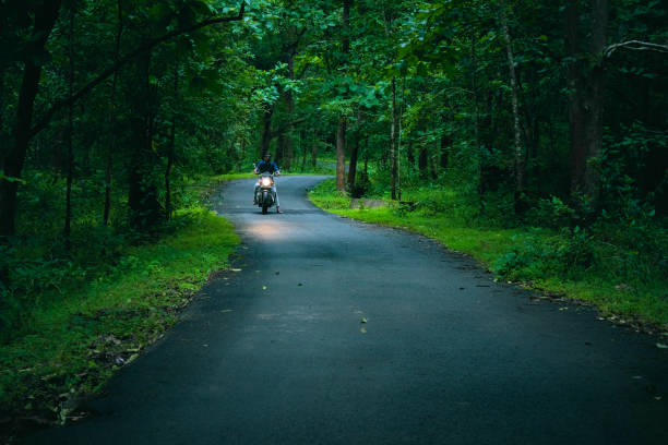 young indian guy with motorbike in the dark rainforest road, at dandeli,karnataka. - indiana autumn woods forest imagens e fotografias de stock