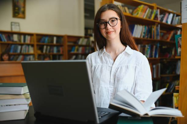 istock in the library - pretty female student with books working in a high school library. 1452455384
