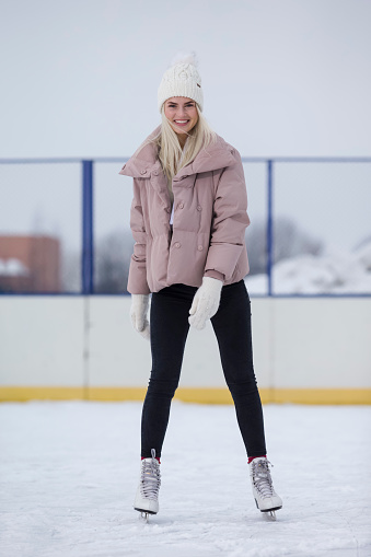 Young Caucasian Girl in Winter With Ice Skates Posing Over a Snowy Winter Landscape Outdoor. Vertical Shot