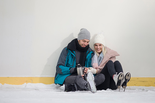 Winsome Happy Caucasian Couple In Love in Winter With Ice Skates Posing Together With Vacuum Flask In Snowy Winter Landscape Outdoor. Horizontal Composition