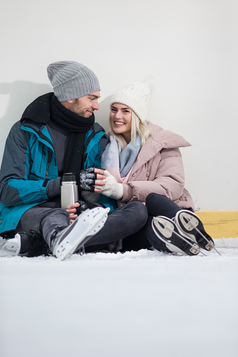 Winsome Happy Caucasian Couple In Love in Winter With Ice Skates Posing Together With Vacuum Flask In Snowy Winter Landscape Outdoor. Vertical image