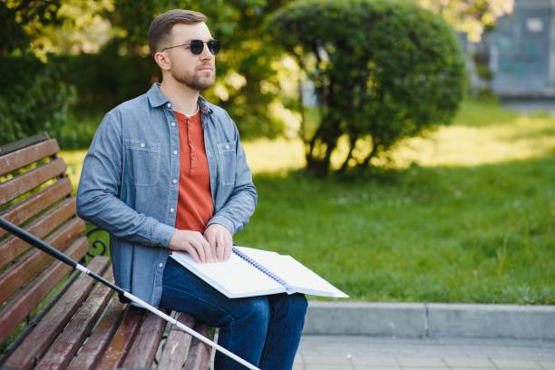 istock Blind man reading book on bench in park 1452456578