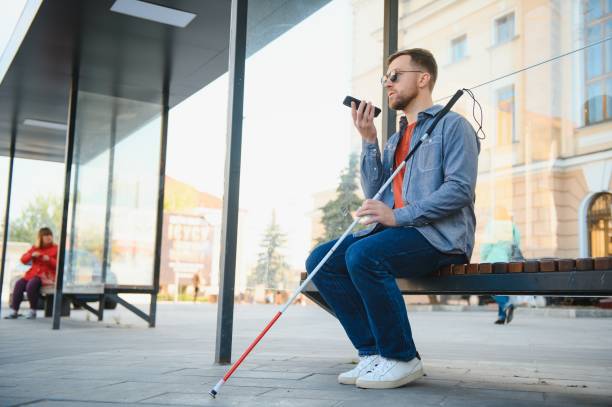 Young blind man with smartphone sitting on bench in park in city, calling. Young blind man with smartphone sitting on bench in park in city, calling blindness stock pictures, royalty-free photos & images