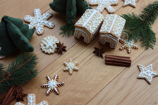 Small Gingerbread houses with many gingerbread cookies in shape of stars and snowflake  on wooden table with pine branches, cinnamon and star anise spices on selective focus