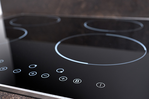 Modern induction electric hob cooker with control panel buttons. Electric hob detail closeup. Stove top panel controls of modern kitchen. Electric hob ceramic surface, and touch control panel.