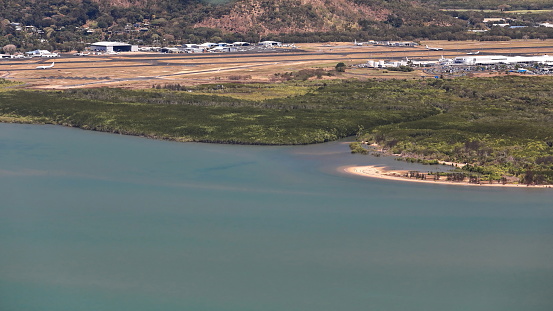 Aerial view of Cairns International Airport main runway lined by hangars and terminals and traversed by a coastal creek coming from the nearby Mount Whitfield and the Aeroglen suburb. Cairns-QLD-AUS
