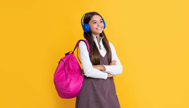 istock cheerful child in headphones with school backpack on yellow background 1452465672