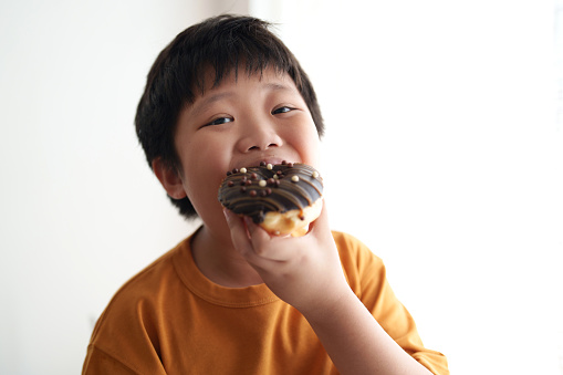 Hungry Asian boy enjoying doughnut at home