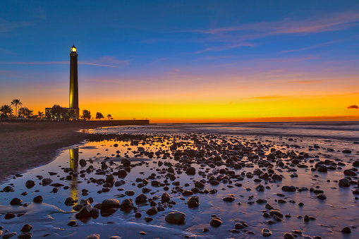 Lighthouse of Maspalomas At Gran canaria Island Known as  Faro de Maspalomas at Sunset During Blue Hour With Sea And Stones. Horizontal image