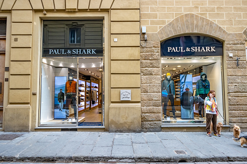 A woman on the phone walking her dogs outside Paul & Shark Clothing Store in Florence at Tuscany, Italy
