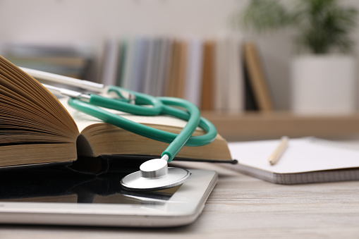 Book, tablet and stethoscope on wooden table indoors, closeup with space for text. Medical education