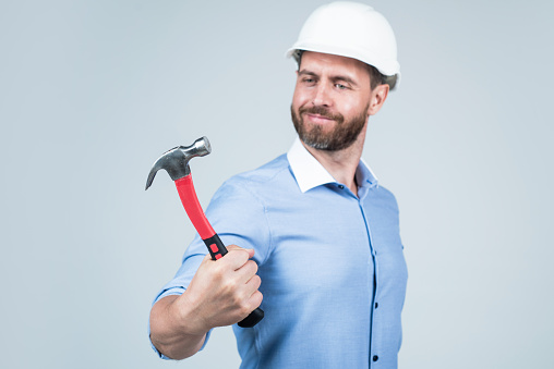 handsome smiling bearded businessman in helmet hold hammer, repairing.