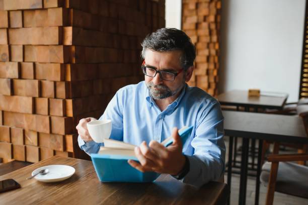 istock Mature handsome man reading a book in a cafe 1452470437
