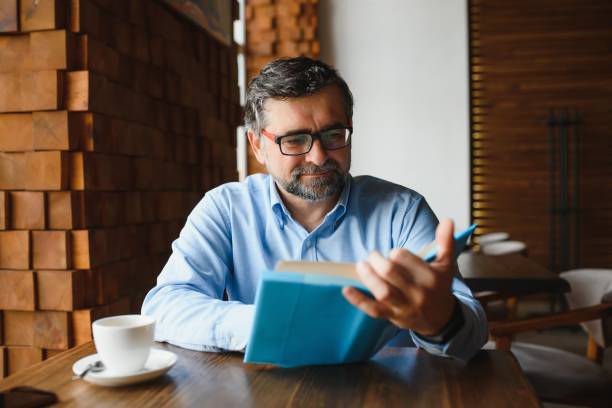 istock Mature handsome man reading a book in a cafe 1452470449