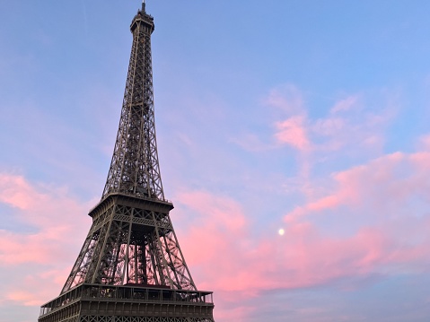 Cotton candy clouds and a view of the moon during sunset at the Eiffel Tower in Paris, France.