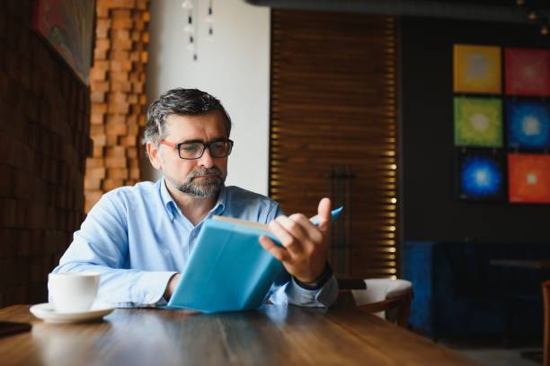 bel homme mûr lisant un livre dans un café - restaurant business person setting the table clothing photos et images de collection