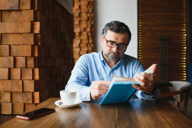 istock Mature handsome man reading a book in a cafe 1452470519