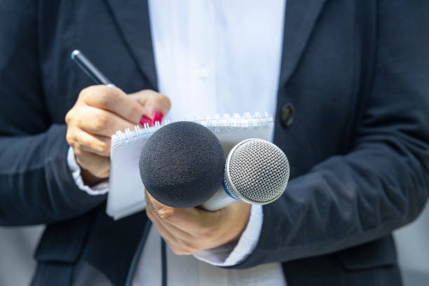Female journalist at press conference or media event, holding microphone and writing news stock photo