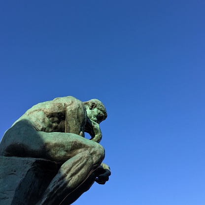Looking up at The Thinker against a clear blue sky at the Rodin Museum in Paris, France.