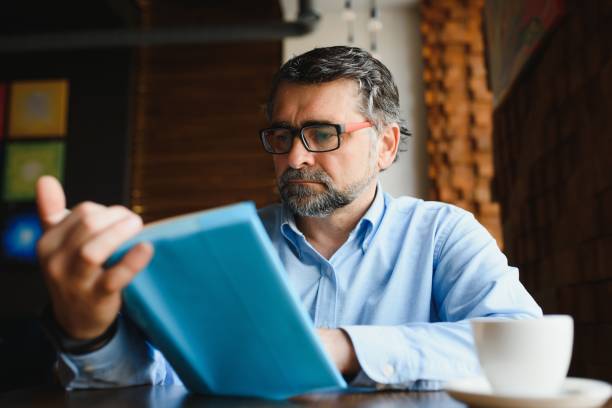 istock Mature handsome man reading a book in a cafe 1452470945