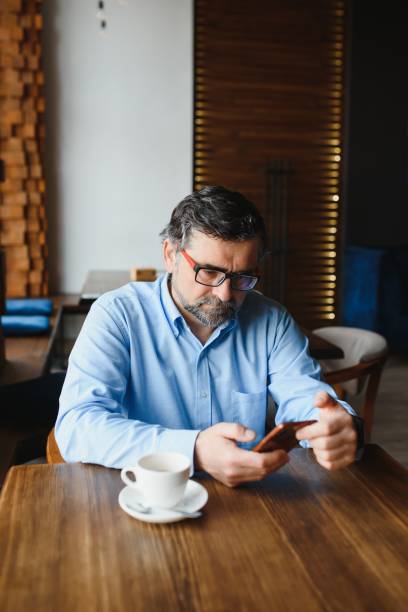 istock Taking time for coffee break. Confident mature man in formalwear drinking coffee and typing a message on mobile phone while sitting in restaurant 1452470953