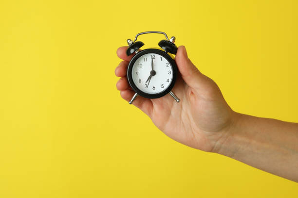 istock Female hand holds alarm clock on yellow background 1452473019