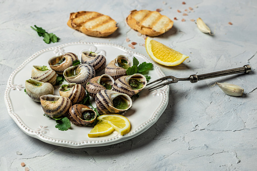 Escargots de Bourgogne Snails with herbs, butter, garlic, glass of white wine on a light background, gourmet food. Restaurant menu, Traditional French cuisine,